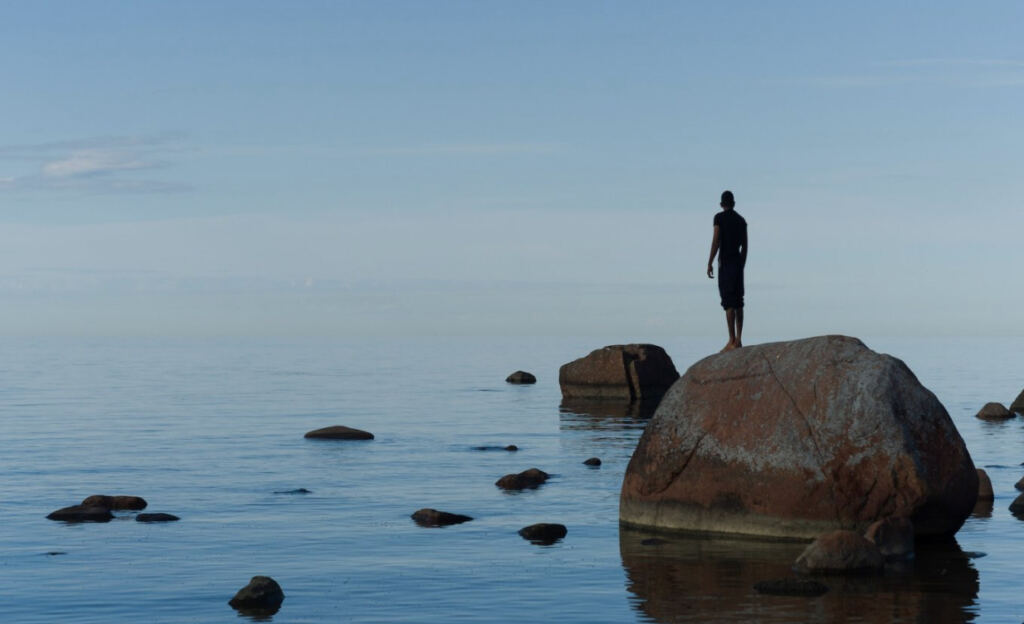 persona su uno scoglio guarda verso il mare calmo