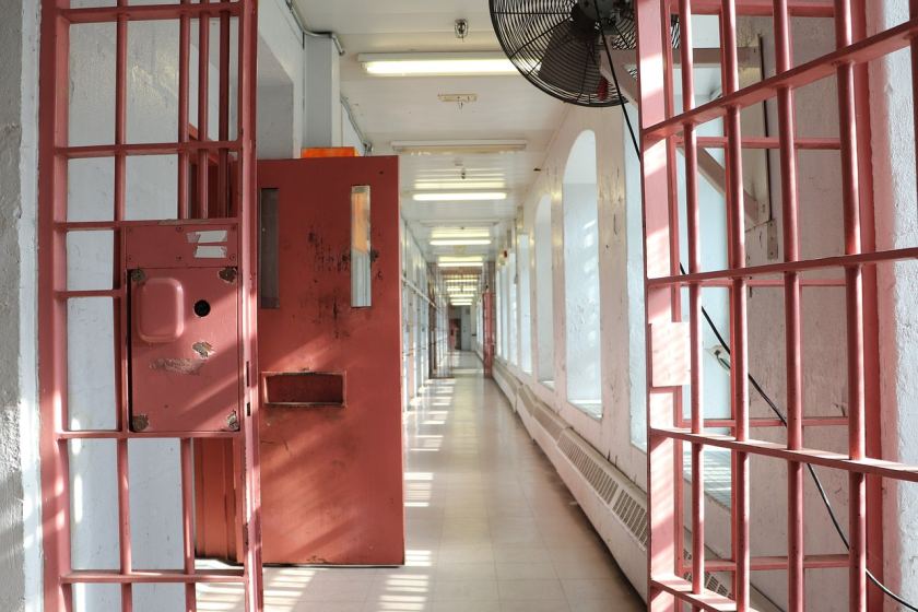 interno di un carcere, corridoio a cui si accede da una porta aperta e sbarre rosse
