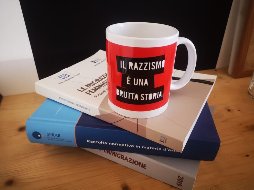 Tazza con scritta Il razzismo è una brutta storia su una pila di libri sull'immigrazione e asilo